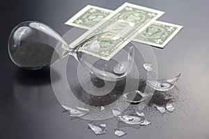 Broken hourglass on the background of banknotes. loss of time and finances. end of earning opportunities