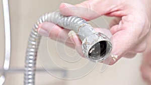 Broken leaky shower hose from a bathtub faucet covered with limescale in female hands close up