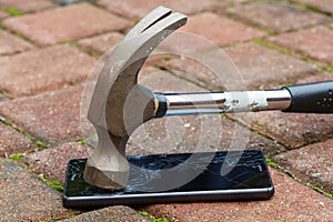 Broken mobile phone hit by hammer lying on pavement
