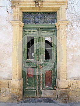 Broken old double green doors with rusty letterbox in an abandoned derelict house with broken windows and faded peeling paint