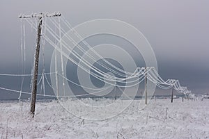 Broken phase electrical power lines with hoarfrost on the wooden electric poles on countryside in the winter after storm