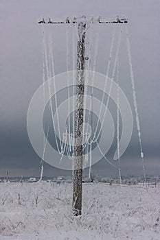 Broken phase electrical power lines with hoarfrost on the wooden electric poles on countryside in the winter after storm