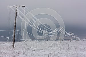 Broken phase electrical power lines with hoarfrost on the wooden electric poles on countryside in the winter after storm photo