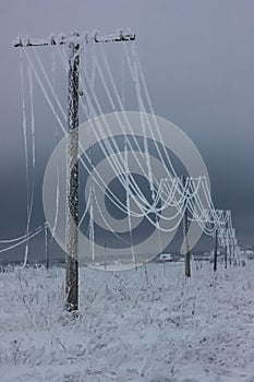 Broken phase electrical power lines with hoarfrost on the wooden electric poles on countryside in the winter after storm