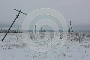 Broken phase electrical power lines with hoarfrost on the wooden electric poles on countryside in the winter after storm