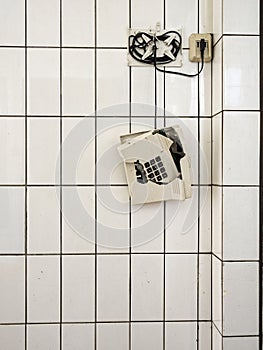 A broken phone hangs by its cord in front of a white tiled wall in an old building