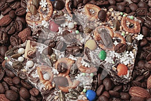 Broken pieces of handmade chocolate with a variety of additives on the background of coffee beans, almonds