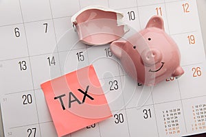 Broken piggy bank on a white calendar background, tax time concept