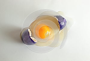 Broken purple eggshell with raw egg. Creative copy space on light background. Minimal Easter concept