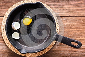 Broken quail egg in a frying pan on a wooden table