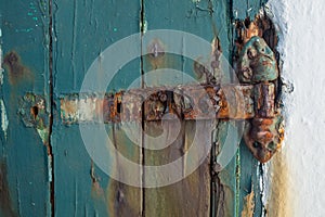 A broken rusting door hinge on a painted wooden door, paint peeling off the wood