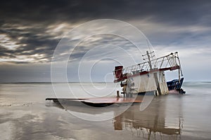 The broken ship along with the sea on a sandy beach and sunset t