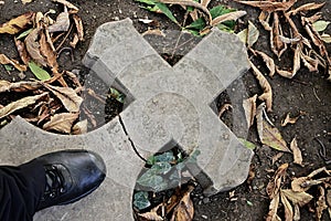 Broken stone cemetery cross lying on ground with black leather boot standing on it photo
