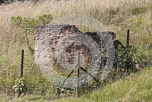 Broken Stone Structure in Long Grass behind Electric Fence