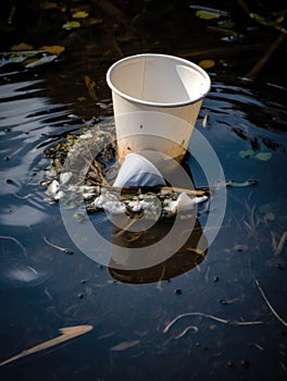 A broken styrofoam cup floating in a polluted lake.. AI generation