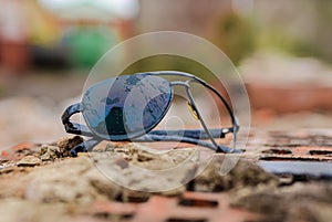 Broken sunglasses lie on a brick flat surface.
