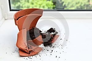 Broken terracotta flower pot with soil on windowsill indoors