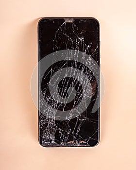 Broken touchscreen black phone, smartphone, broken glass display smartphone on a beige backgroundn
