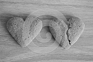 Broken and unbroken shortbread hearts on wooden background black and white as unhappy love background.