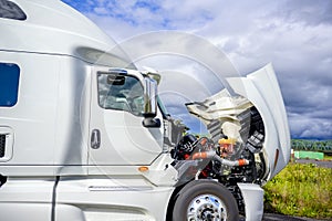 Broken white big rig semi truck tractor stands on the side of the road with an open hood awaiting mobile repair assistance