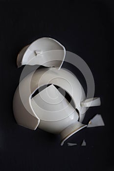 Broken white china cup on black background