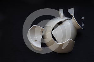 Broken white china cup on black background
