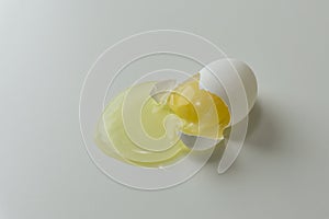 Broken white egg with egg shel and yolk on gray background