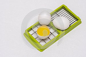 Broken and whole white eggs on green kitchen cutter on a white surface