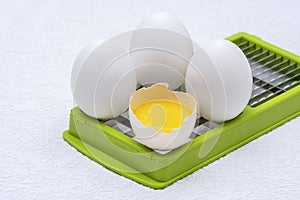 Broken and whole white eggs on green kitchen cutter on a white surface