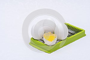 Broken and whole white eggs on green kitchen cutter on a white surface