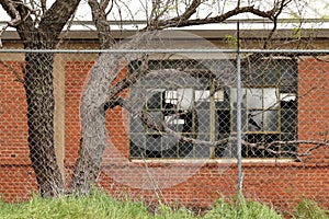 Broken window of abandoned warehouse seen through chainlink fence