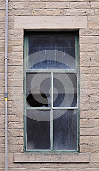 Broken window pane in an old abandoned house with stone walls and green frame