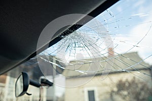 Broken windshield with a lot of cracks and small glass pieces, damaged car