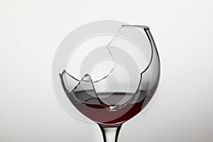 Broken wine glass with red wine on white background