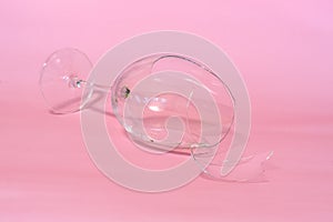 broken wine glass with shards on pink background