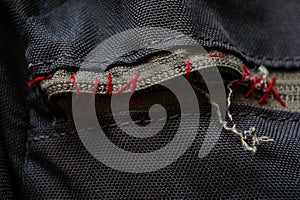 Broken zipper on a backpack sewn in red thread