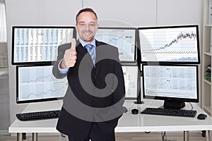 Broker Gesturing Thumbs Up Against Multiple Monitors