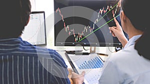 Broker showing some ascending to his colleague planning and analyzing graph stock market trading with stock chart data on multiple