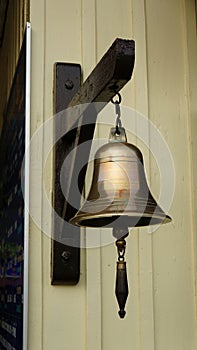 Bronze Bell hanging on wooden dark hook at bright wooden wall