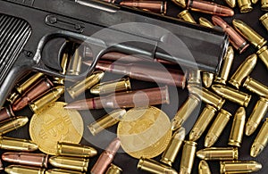 Bronze and brass gun bullets scattered on dark table, black pistol barrel, golden bitcoin coins near - illegal use of