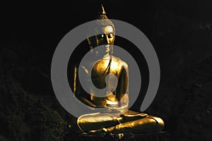 Bronze Buddha statue praying in lotus pose inside a cave.