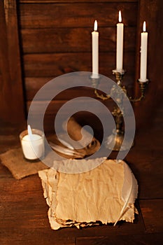 Bronze candlestick with three burning candles on a wooden brown table. Old parchment.