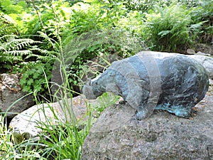 Bronze cat statue on the  stones, creek, bushes in the summer   park,  in Kotka, Finland