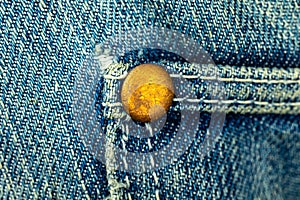Bronze metal rivet on a blue denim jeans with stitched seam of pocket, close-up background