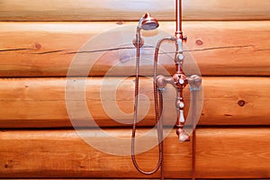 Bronze mixer tap in retro style on log wall in bathhouse