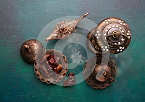 Bronze plate with dates, coffee cup, arabic lantern and aladdin lamp on dark green wooden background. Ramadan kareem. Ramadan