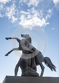 Bronze sculpture of athlete taming horse  at an Anichkov bridge in St. Petersburg against the blue sky