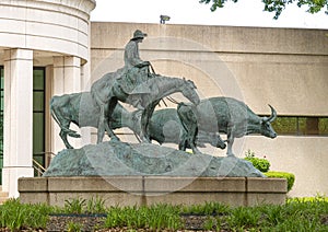 Bronze sculpture by unidentified artist featuring a cowboy on a horse herding cattle.