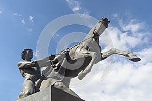 Bronze sculpture of young man taming horse at an Anichkov bridge in St. Petersburg against the blue sky with light clouds