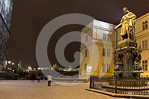 Bronze statue of the eleventh Czech King and Roman Emperor Charles IV. in night snowy Prague with Prague Castle near Charles Bridg